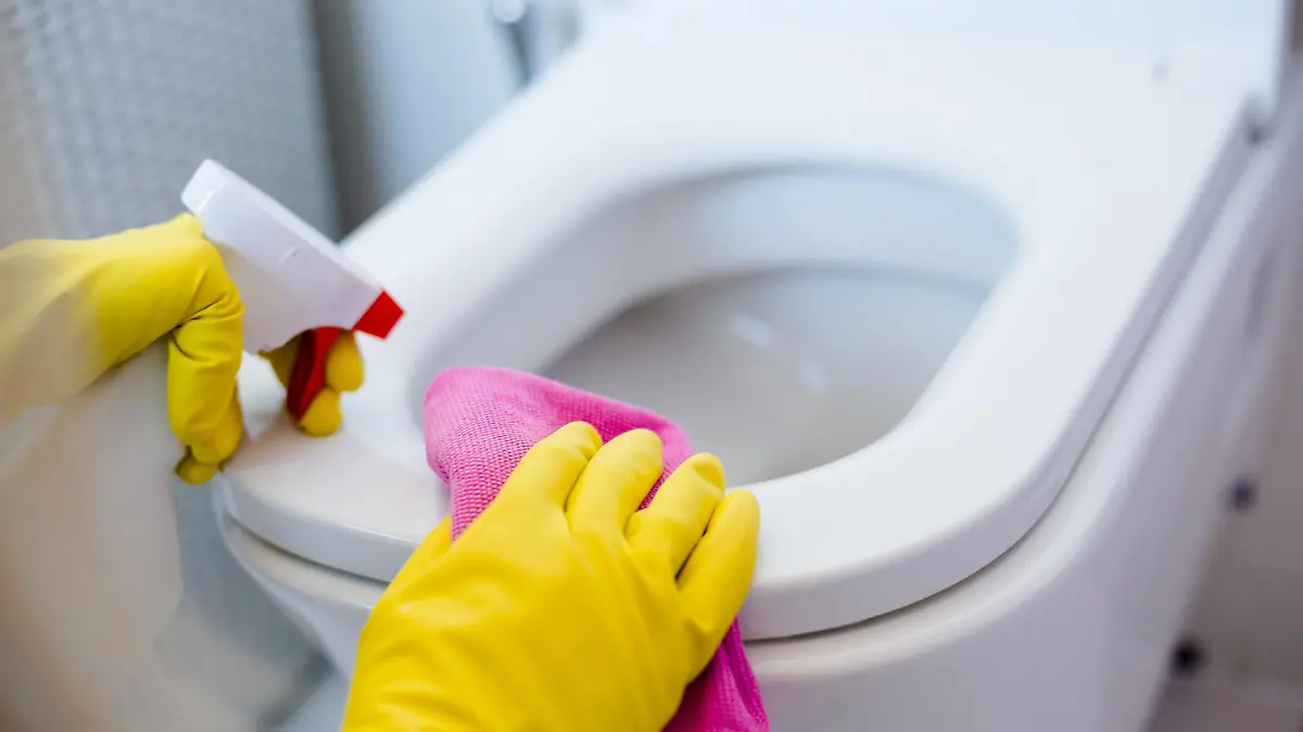 Woman in yellow rubber gloves cleaning toilet with pink cloth