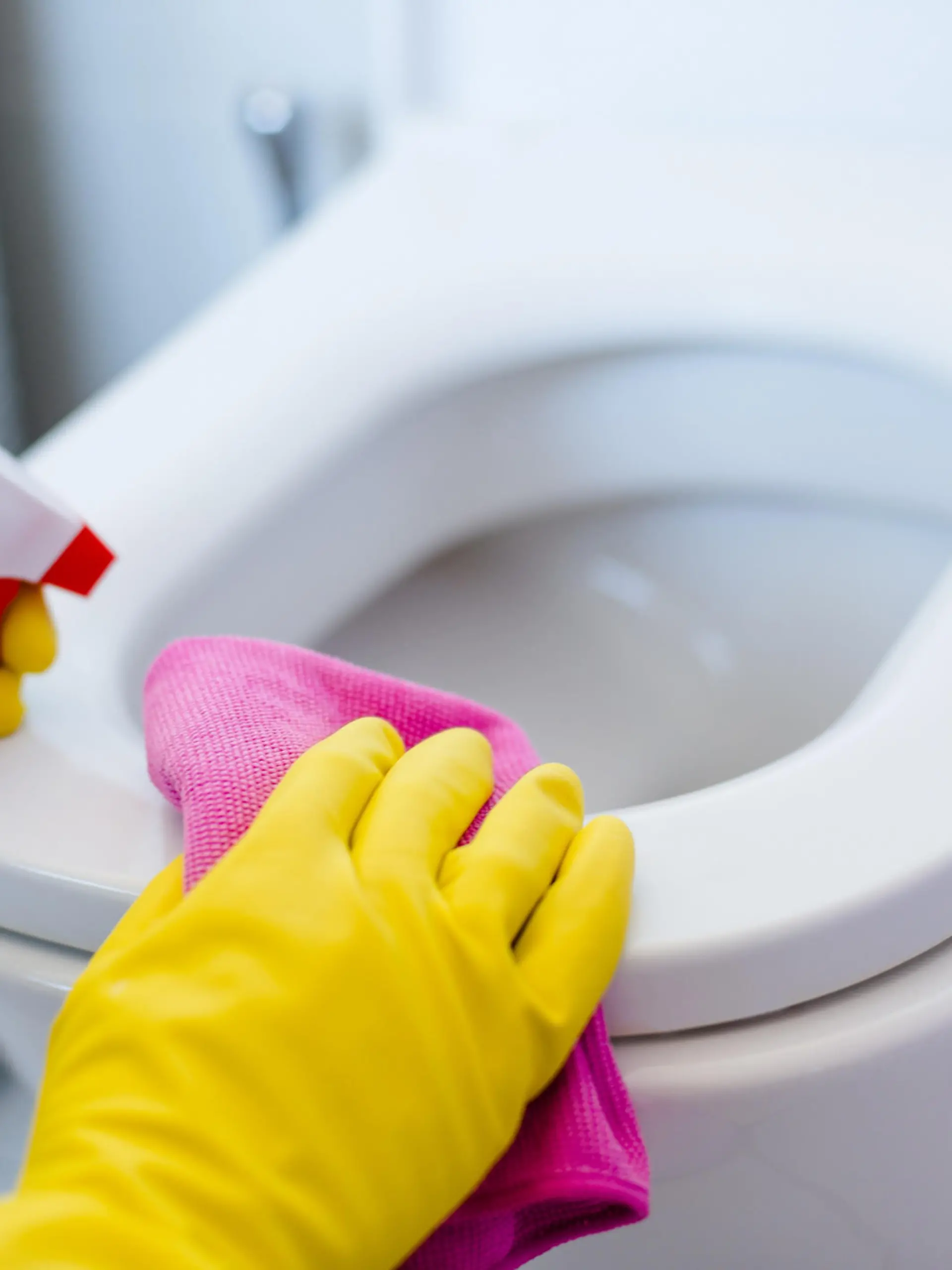 Woman in yellow rubber gloves cleaning toilet with pink cloth