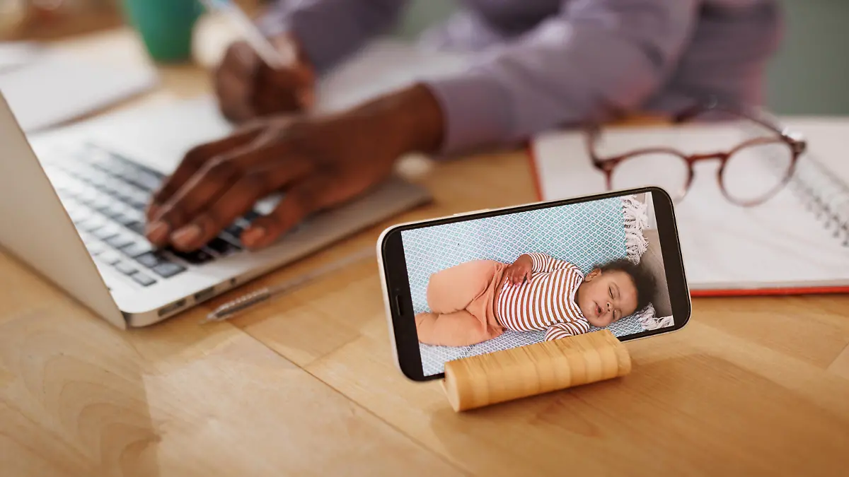 Close up shot of baby monitor mobile app while mother is using laptop in the background