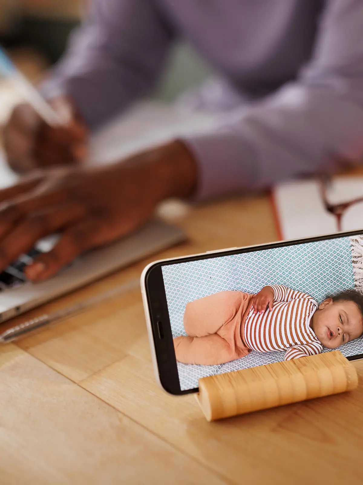 Close up shot of baby monitor mobile app while mother is using laptop in the background