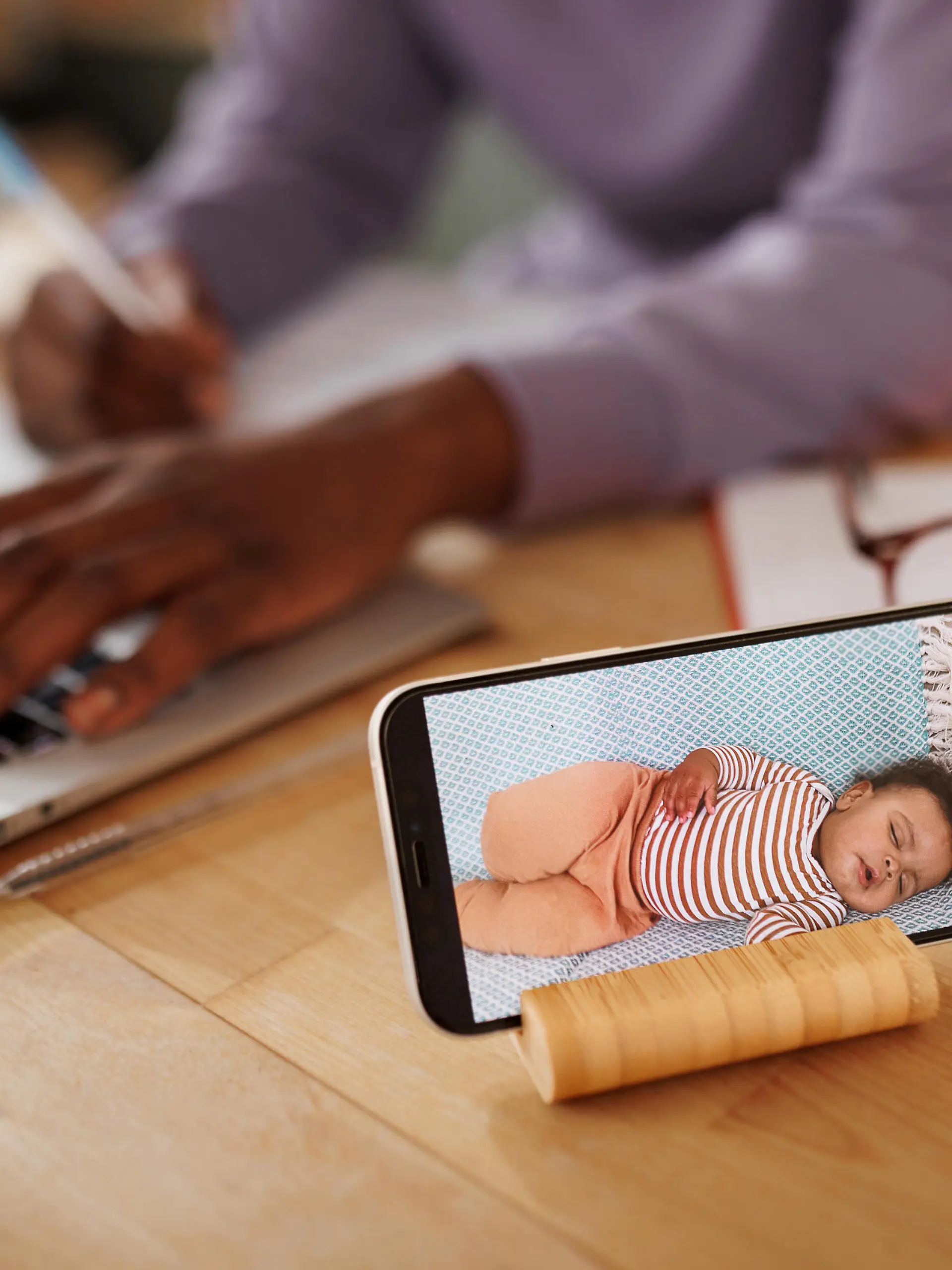Close up shot of baby monitor mobile app while mother is using laptop in the background