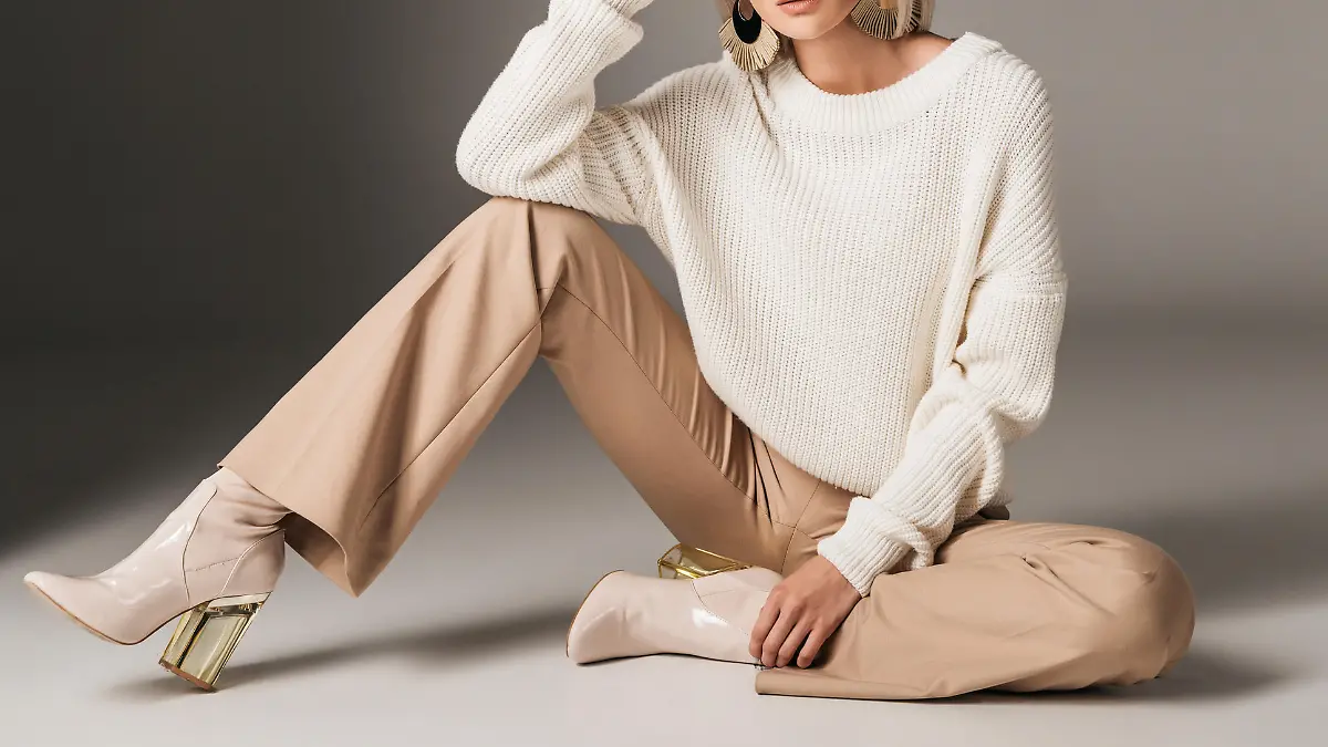 attractive fashionable woman posing in white trendy sweater, beige pants and autumn heels, on grey