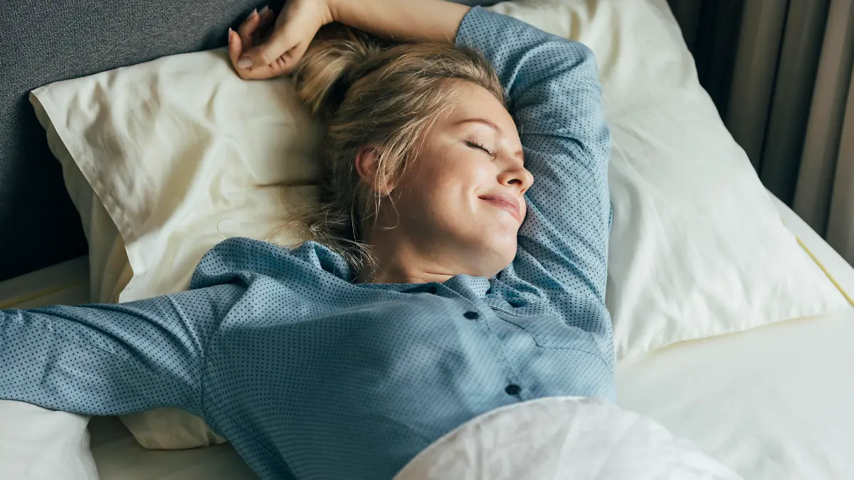 Beautiful smiling blonde woman in blue pyjamas waking up well rested on a sunny morning.
