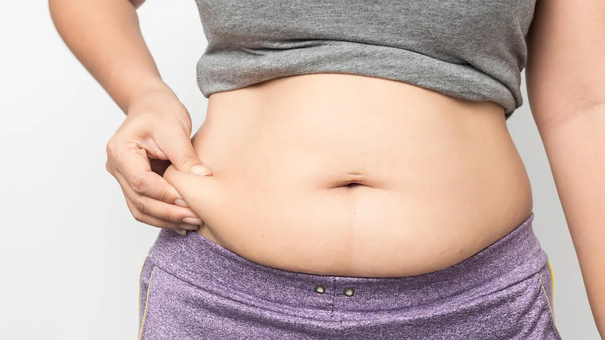 Overweight woman hand pinching excessive belly fat on gray background, Healthy concept
