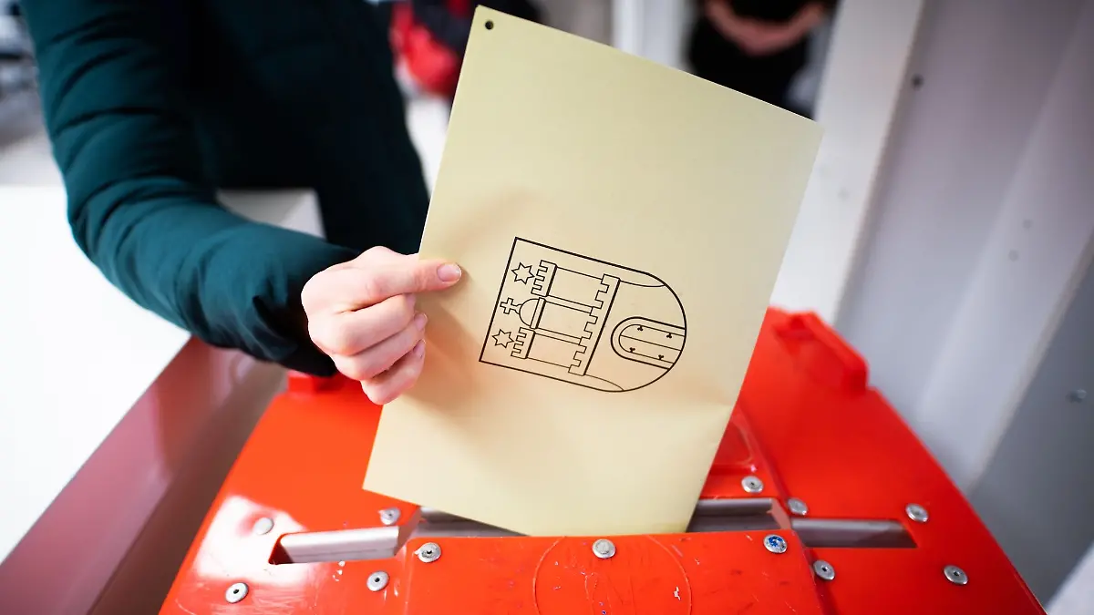 Eine Frau hält einen Stimmzettel an eine Wahlurne.