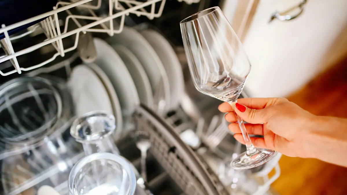 Close up image of a young woman's hand taking a clean wine glass out of the dishwasher machine in her apartment in Paris, France. House work, domestic work concepts in a modern, French kitchen.