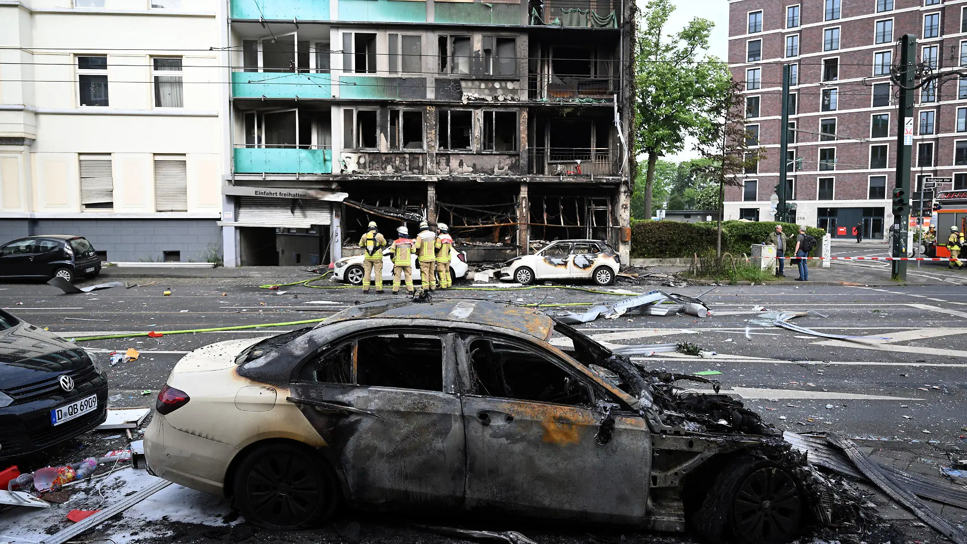 ARCHIV - 16.05.2024, Nordrhein-Westfalen, Düsseldorf: Feuerwehrleute stehen vor einem Wohnhaus, in dem ein Brand wütete. Bei dem Brand in Düsseldorf sind mehrere Menschen ums Leben gekommen und weitere verletzt worden. Wie die Feuerwehr mitteilte, war in der Nacht zum Donnerstag aus bislang ungeklärter Ursache ein in einem Wohnhaus integrierter Kiosk in Brand geraten. (zu dpa: «Explosion in Düsseldorf mit drei Toten: Frau in kritischem Zustand») Foto: Federico Gambarini/dpa +++ dpa-Bildfunk +++