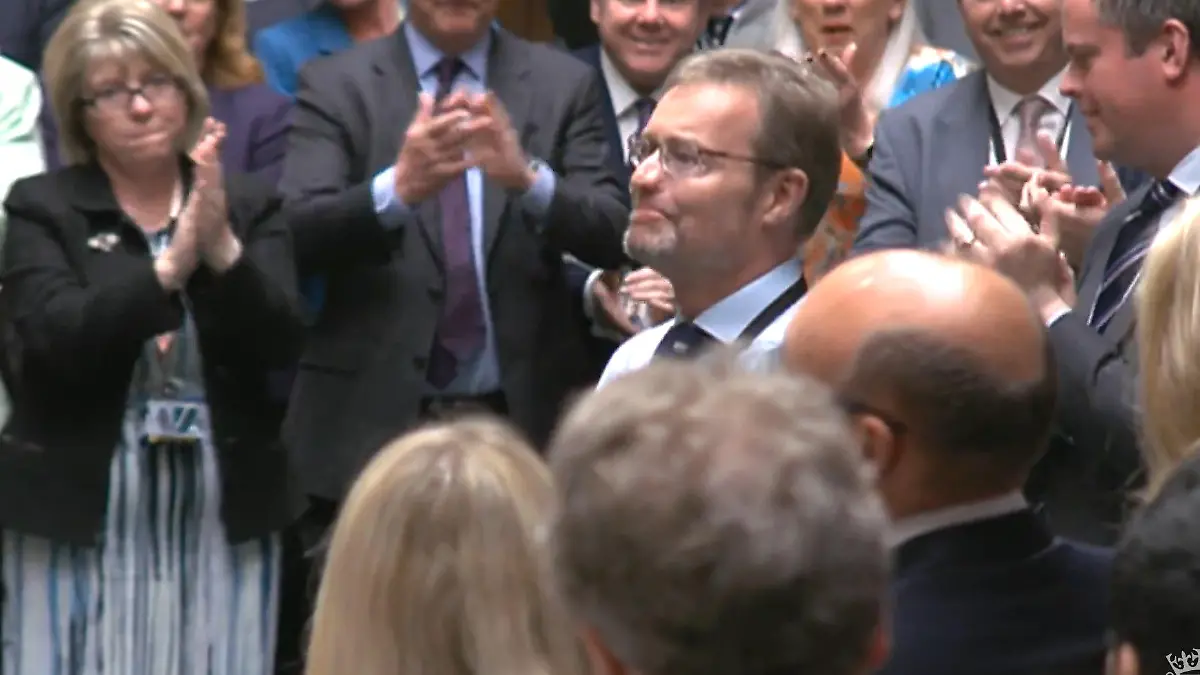 SCREENSHOT - 22.05.2024, Großbritannien, London: HANDOUT - Craig Mackinlay (M), konservativer Abgeordneter für South Thanet, wird von den Mitgliedern des Parlaments beklatscht, als er zum ersten Mal ins Unterhaus zurückkehrt, seit er am 28. September mit einer Sepsis ins Krankenhaus eingeliefert wurde, in deren Folge ihm beide Hände und Füße amputiert werden mussten. Foto: House Of Commons/Uk Parliament/PA Wire/dpa - ACHTUNG: Nur zur redaktionellen Verwendung im Zusammenhang mit der aktuellen Berichterstattung und nur mit vollständiger Nennung des vorstehenden Credits +++ dpa-Bildfunk +++