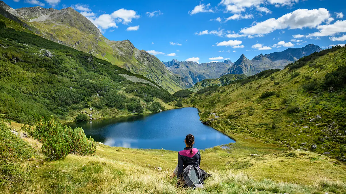 Frau sitzt an einem See in den Bergen.