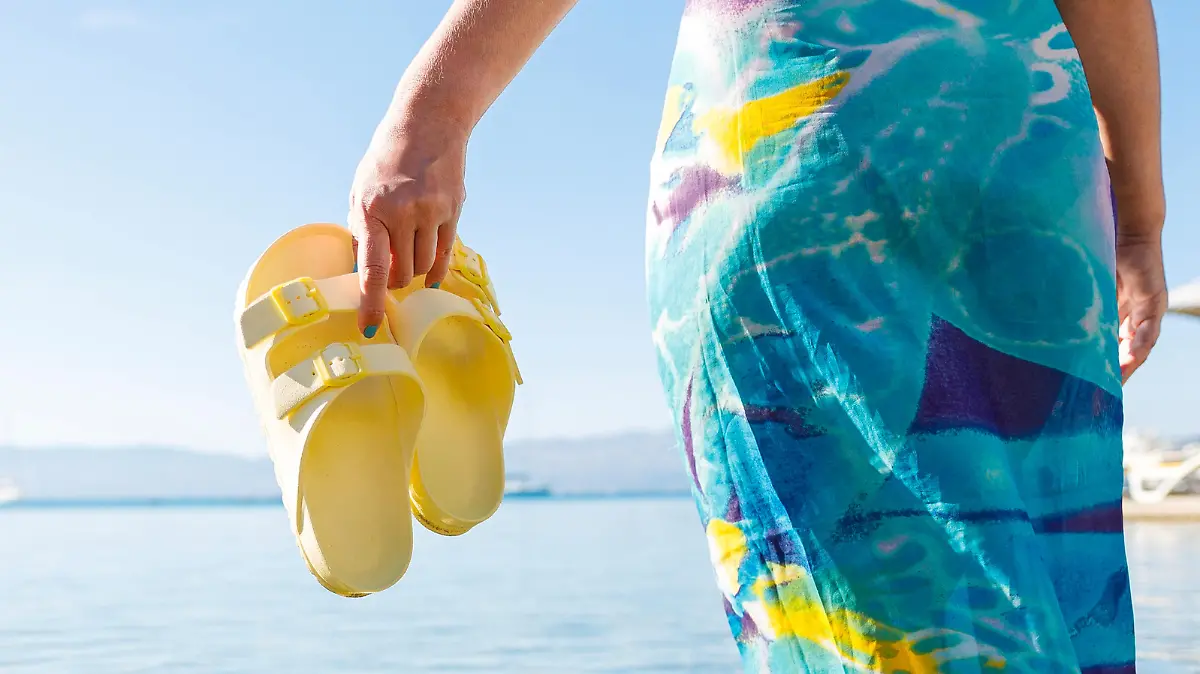 Frau mit Sandalen am Strand.