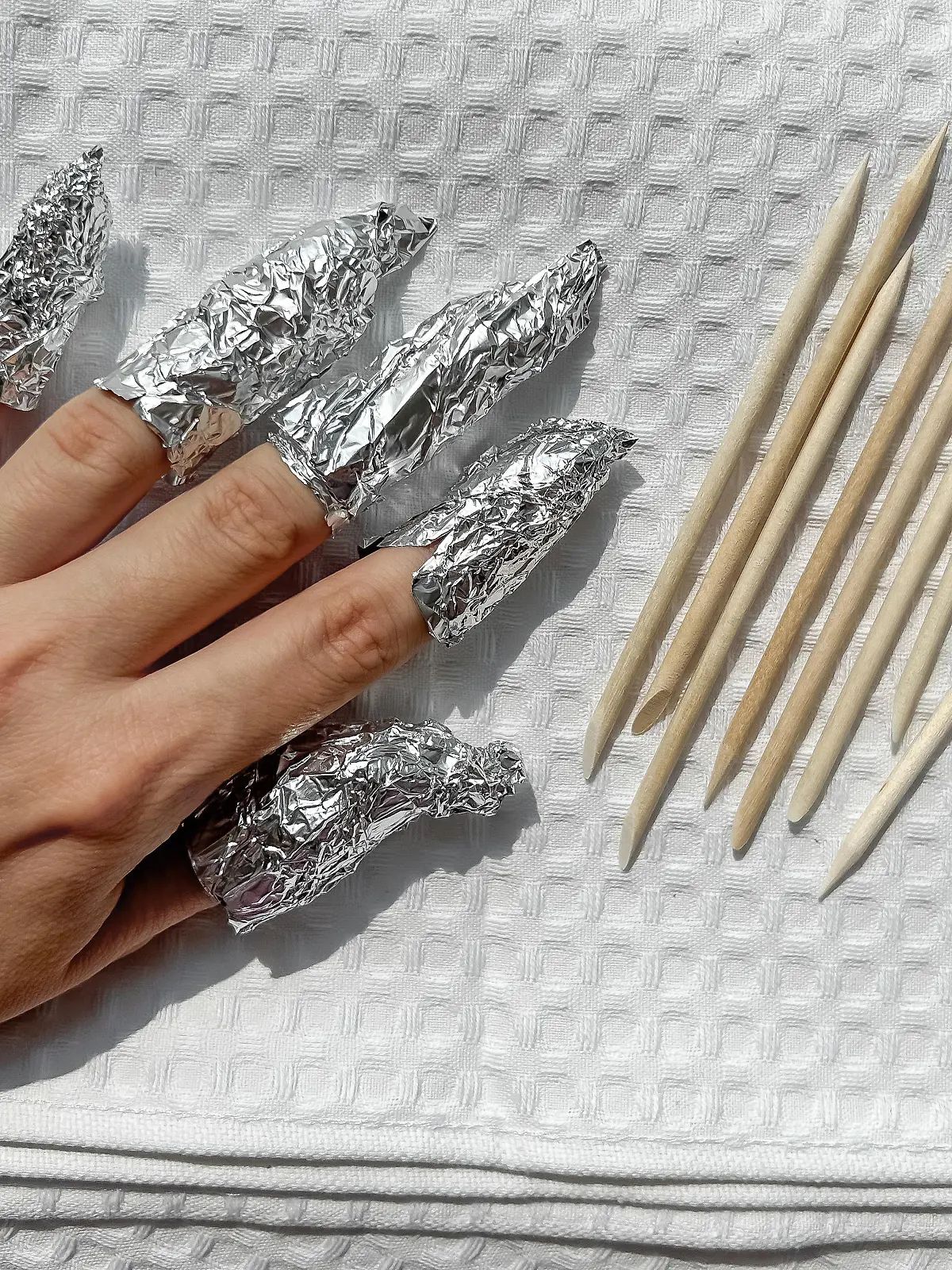 The process of removing gel polish from nails. Nails wrapped in foil on a white towel.