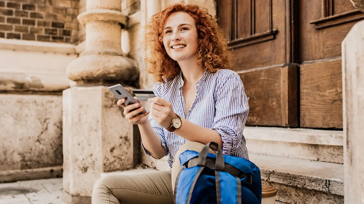 Young female tourist taking a break in the city while holding a mobile phone and credit car