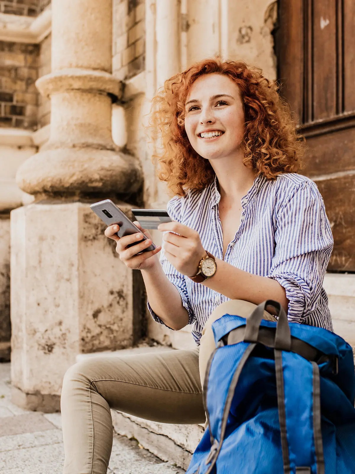 Young female tourist taking a break in the city while holding a mobile phone and credit car