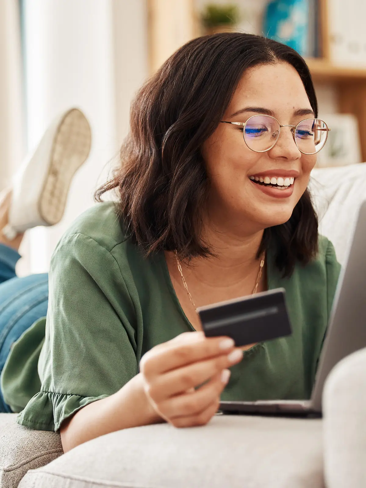 Relax, laptop and credit card, happy woman on couch in living room for internet banking in home for online shopping. Ecommerce payment, smile and cashback, girl on sofa with computer and website sale