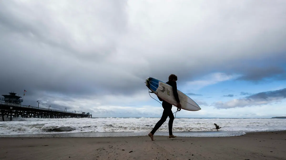 FILE - A surfer heads to the water as storms move through the area in San Clemente, Calif., Dec. 12, 2022. A two-mile (3.2-km) stretch of the popular Southern California beach was closed for the Memorial Day holiday after a shark bumped a surfer off his board the night before, authorities said. The 24-hour closure at San Clemente was announced after the surfer came out of the water and reported the shark’s aggressive behavior to lifeguards Sunday evening, May 26, 2024. (Paul Bersebach/The Orange County Register via AP, File)