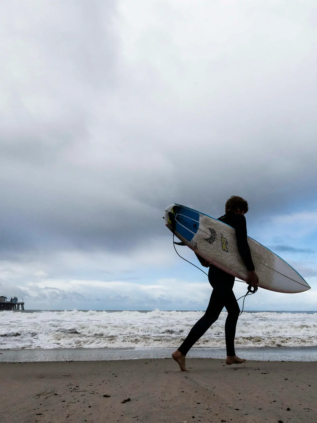 FILE - A surfer heads to the water as storms move through the area in San Clemente, Calif., Dec. 12, 2022. A two-mile (3.2-km) stretch of the popular Southern California beach was closed for the Memorial Day holiday after a shark bumped a surfer off his board the night before, authorities said. The 24-hour closure at San Clemente was announced after the surfer came out of the water and reported the shark’s aggressive behavior to lifeguards Sunday evening, May 26, 2024. (Paul Bersebach/The Orange County Register via AP, File)