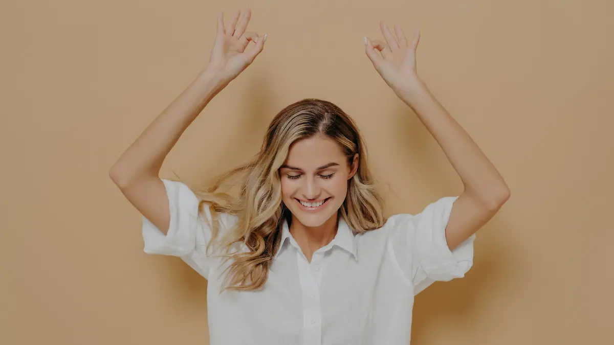 Frau mit weißem Shirt hebt lachend die Arme über den Kopf.