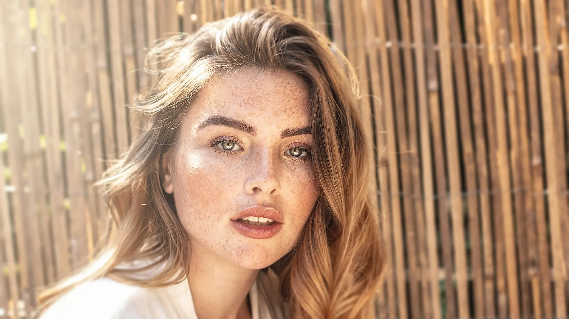 Portrait of young attractive lady with long wavy red hair and freckles on her face. Woman posing on sunny summer day.