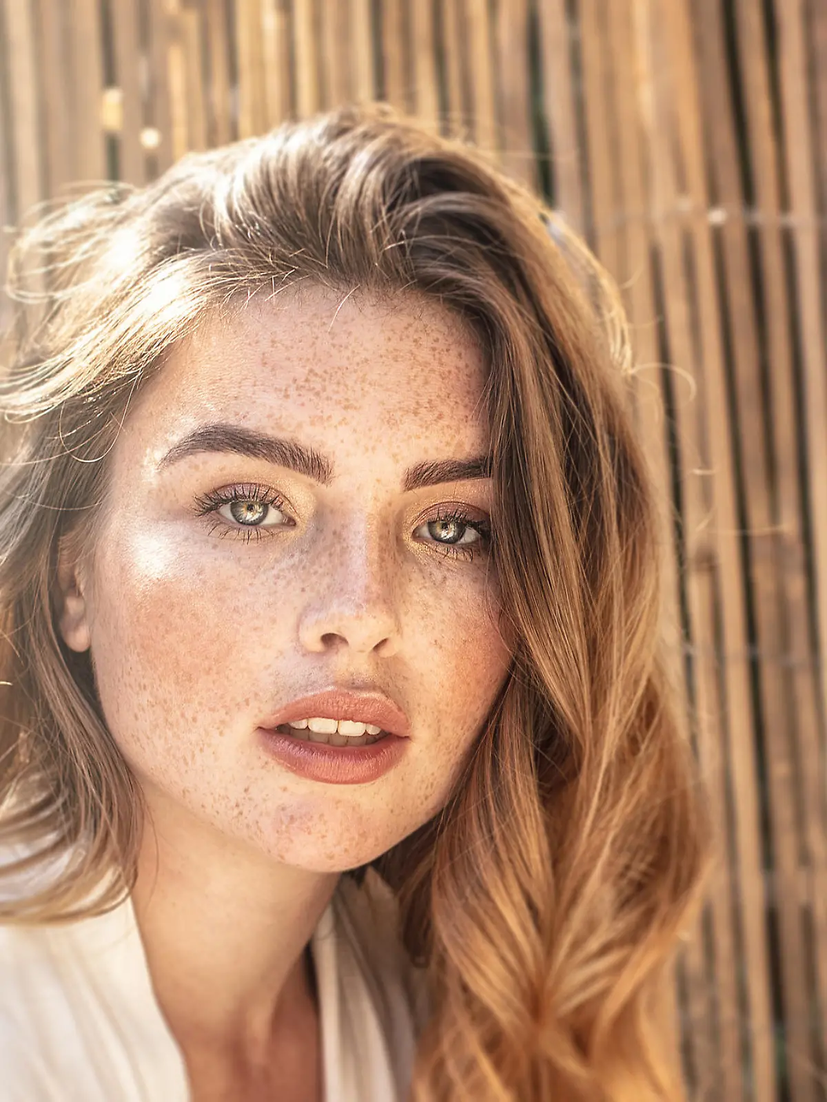 Portrait of young attractive lady with long wavy red hair and freckles on her face. Woman posing on sunny summer day.