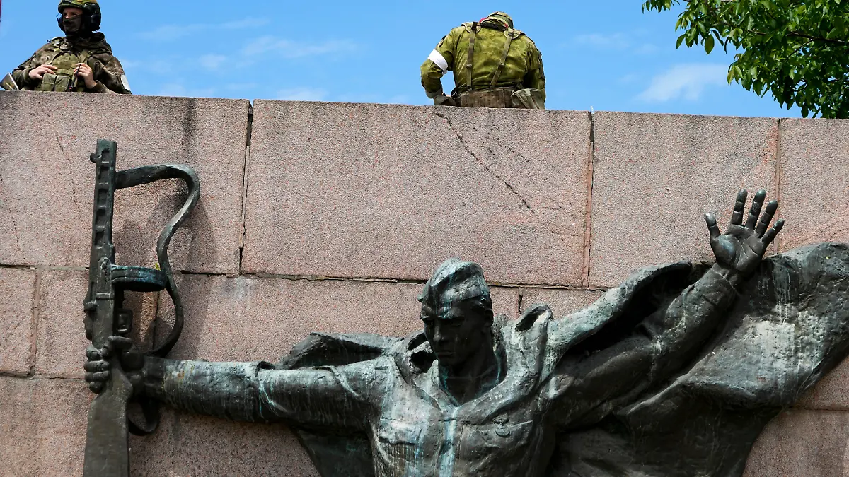 20.05.2022, Ukraine, Kherson: Russische Soldaten bewachen in Cherson, Region Cherson, Südukraine, einen Bereich an der Alley of Glory, Taten der Helden - Einwohner der Region Cherson, die an der Befreiung der Region von den Nazi-Invasoren teilgenommen haben, mit der Skulptur eines sowjetischen Soldaten aus dem Zweiten Weltkrieg im Vordergrund. Die Region Cherson steht seit den Anfängen der russischen Militäraktion in der Ukraine unter der Kontrolle der russischen Streitkräfte. Dieses Foto wurde während einer vom russischen Verteidigungsministerium organisierten Reise aufgenommen. Foto: Uncredited/AP/dpa +++ dpa-Bildfunk +++