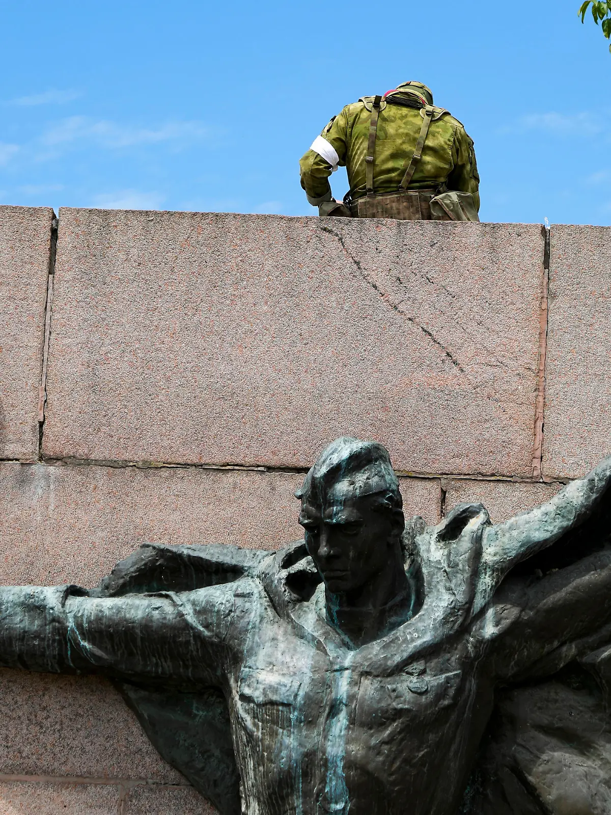 20.05.2022, Ukraine, Kherson: Russische Soldaten bewachen in Cherson, Region Cherson, Südukraine, einen Bereich an der Alley of Glory, Taten der Helden - Einwohner der Region Cherson, die an der Befreiung der Region von den Nazi-Invasoren teilgenommen haben, mit der Skulptur eines sowjetischen Soldaten aus dem Zweiten Weltkrieg im Vordergrund. Die Region Cherson steht seit den Anfängen der russischen Militäraktion in der Ukraine unter der Kontrolle der russischen Streitkräfte. Dieses Foto wurde während einer vom russischen Verteidigungsministerium organisierten Reise aufgenommen. Foto: Uncredited/AP/dpa +++ dpa-Bildfunk +++