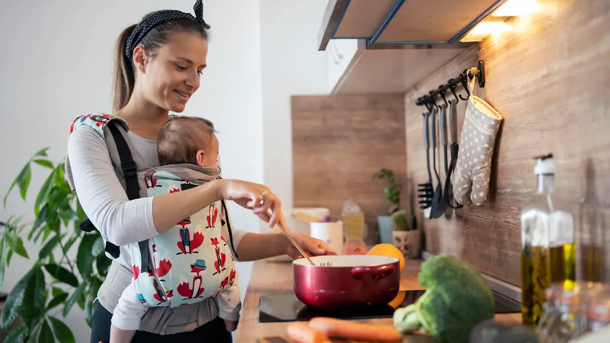 Multi-tasking mother in the kitchen cooking and taking care of her newborn son.