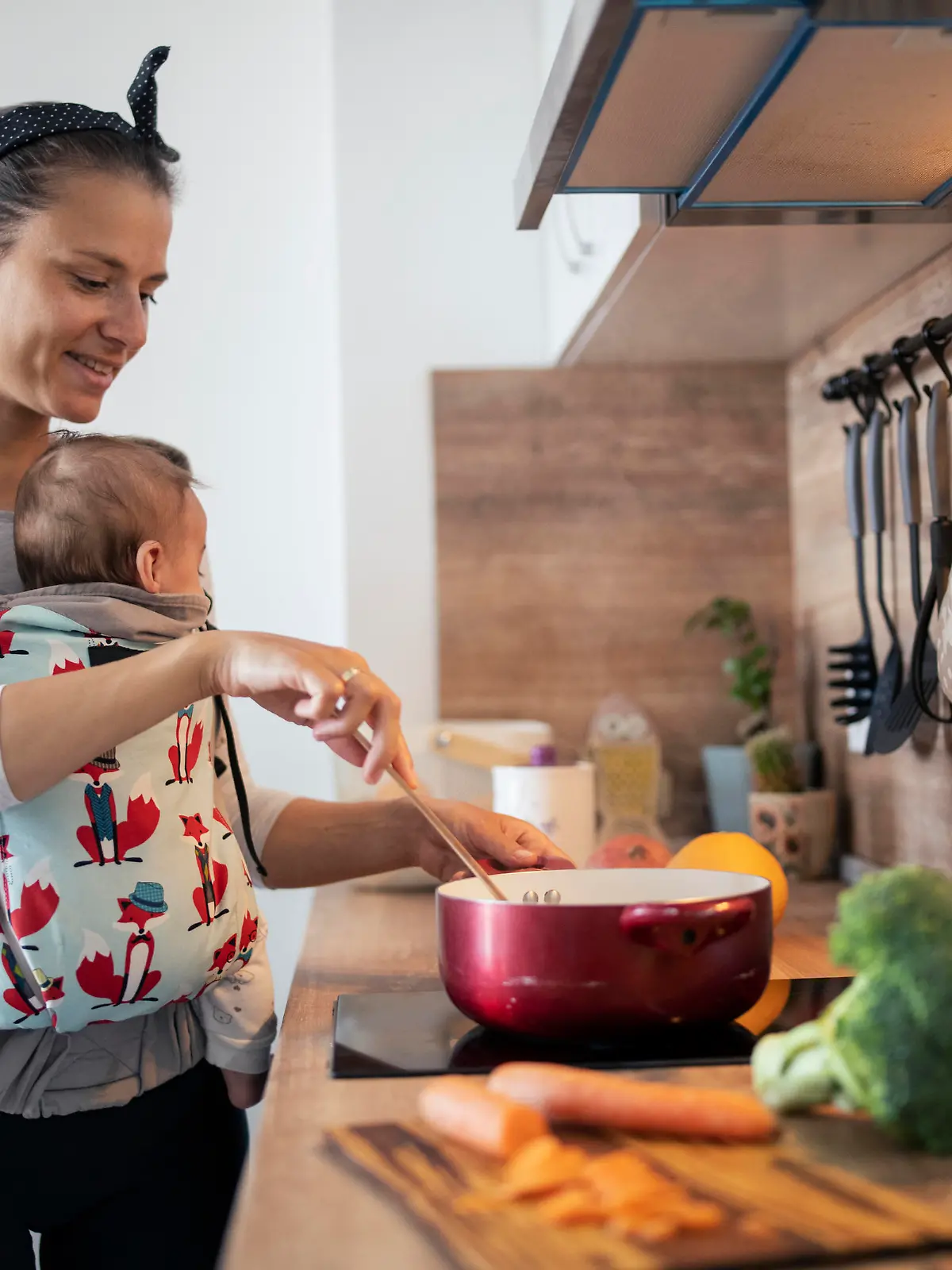 Multi-tasking mother in the kitchen cooking and taking care of her newborn son.