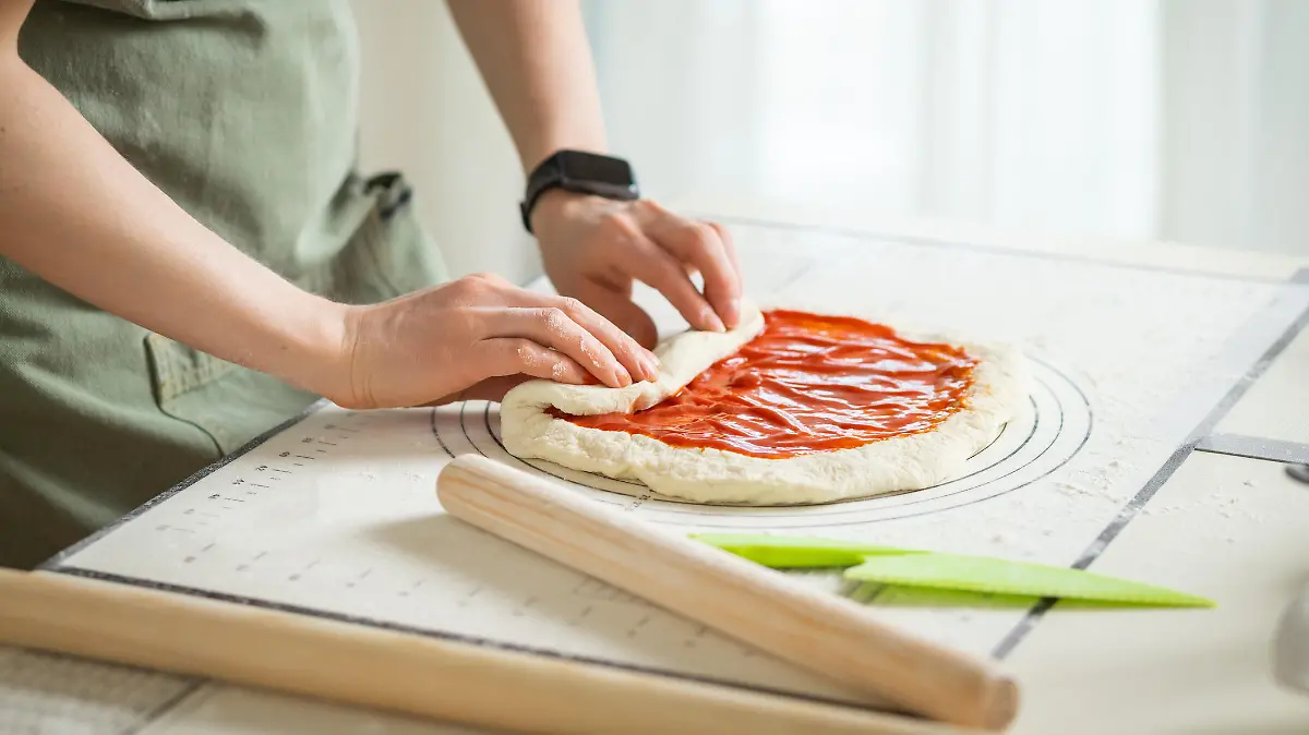 Frau macht Pizza auf einer Backmatte.