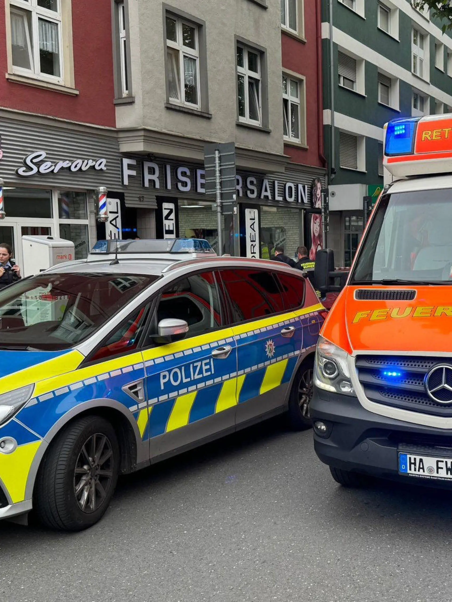 dpatopbilder - ARCHIV - 01.06.2024, Nordrhein-Westfalen, Hagen: Ein Einsatzfahrzeug der Polizei und ein Rettungswagen der Feuerwehr stehen vor einem Friseursalon. In Hagen sind am Samstagmittag an zwei Orten mehrere Schüsse gefallen und mehrere Personen verletzt worden. Die Polizei Hagen bestätigte auf dpa-Anfrage erste Medienberichte, dass es sich bei einem der Tatorte um einen Friseursalon im Stadtteil Eilpe handele. Einsatzkräfte seien mit einem Großaufgebot vor Ort. Foto: Alex Talash/dpa - ACHTUNG: Person(en) wurde(n) aus rechtlichen Gründen gepixelt +++ dpa-Bildfunk +++