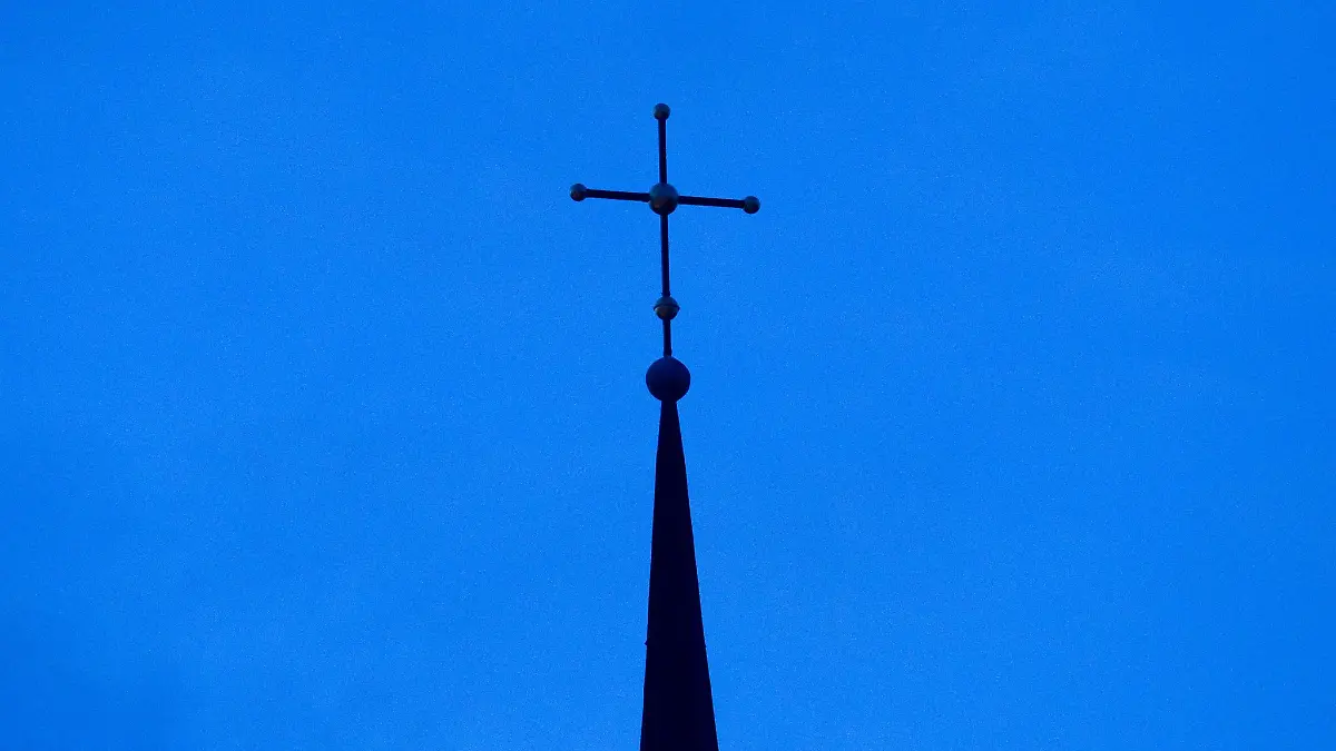 Das Kreuz einer evangelisch-lutherischen Kirche ist in der Abenddämmerung zu sehen.