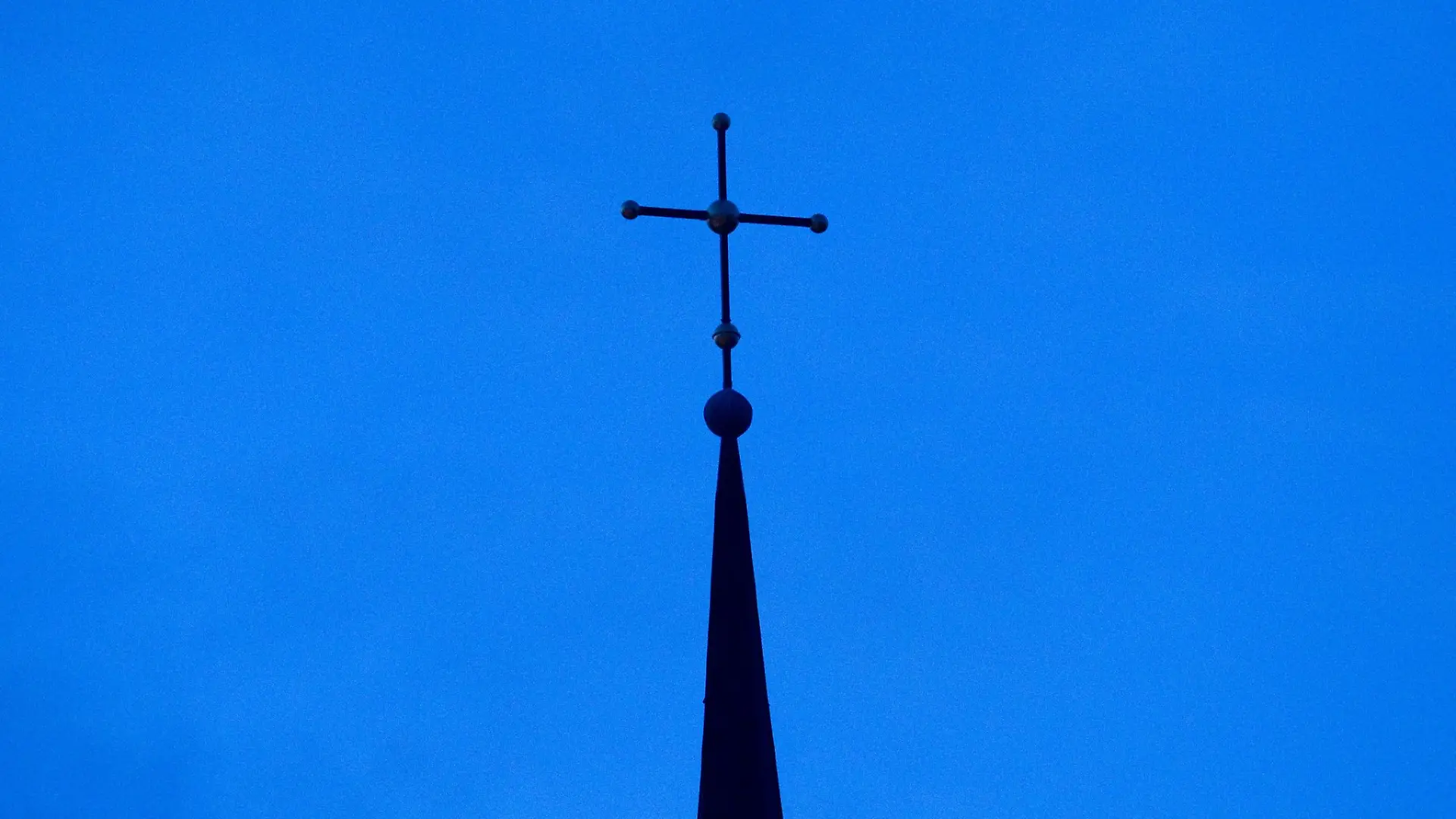 Das Kreuz einer evangelisch-lutherischen Kirche ist in der Abenddämmerung zu sehen.