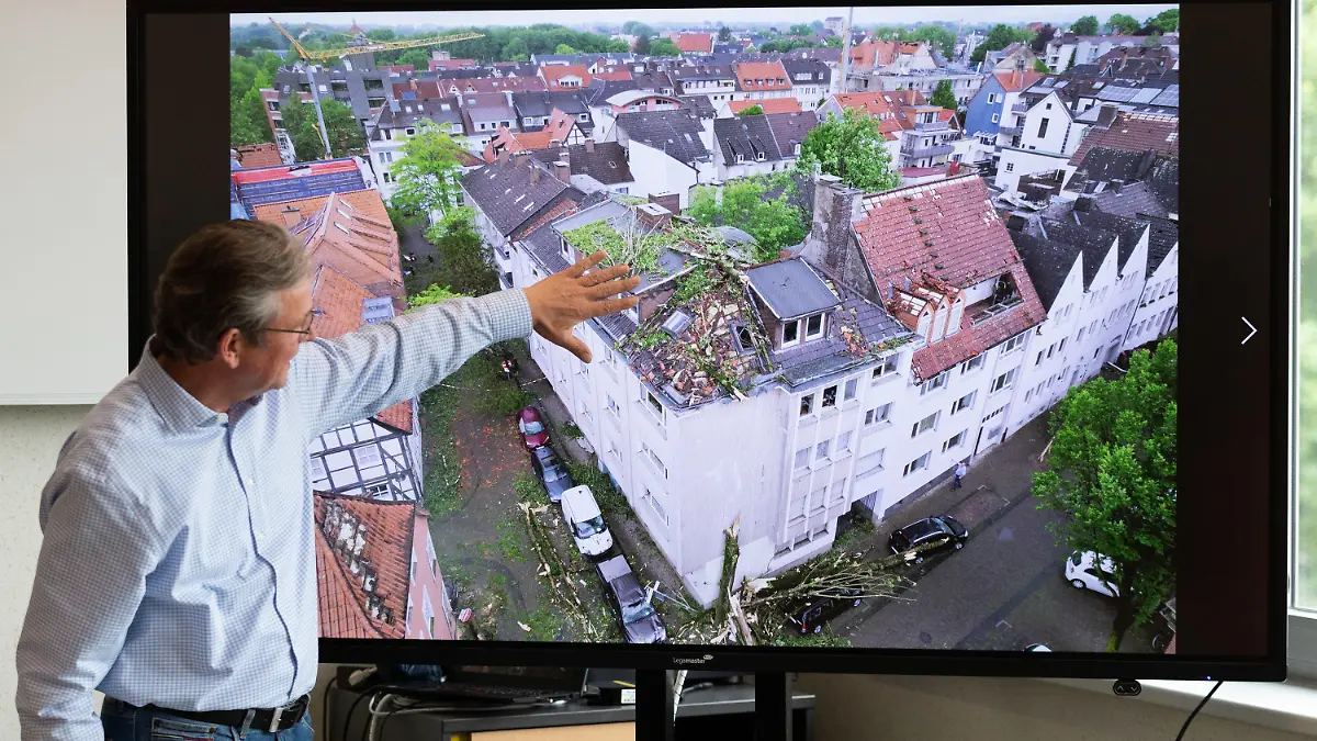 21.05.2022, Nordrhein-Westfalen, Paderborn: Der Bürgermeister von Paderborn, Michael Dreier, spricht bei einer Pressekonferenz vor einem Display mit einem Schadensbild aus der Innenstadt, das zeigt wie Bäume auf ein Hausdach geweht worden sind. Ein Tornado hat in Paderborn und Lippstadt am Freitagnachmittag massive Schäden verursacht. Foto: Friso Gentsch/dpa +++ dpa-Bildfunk +++