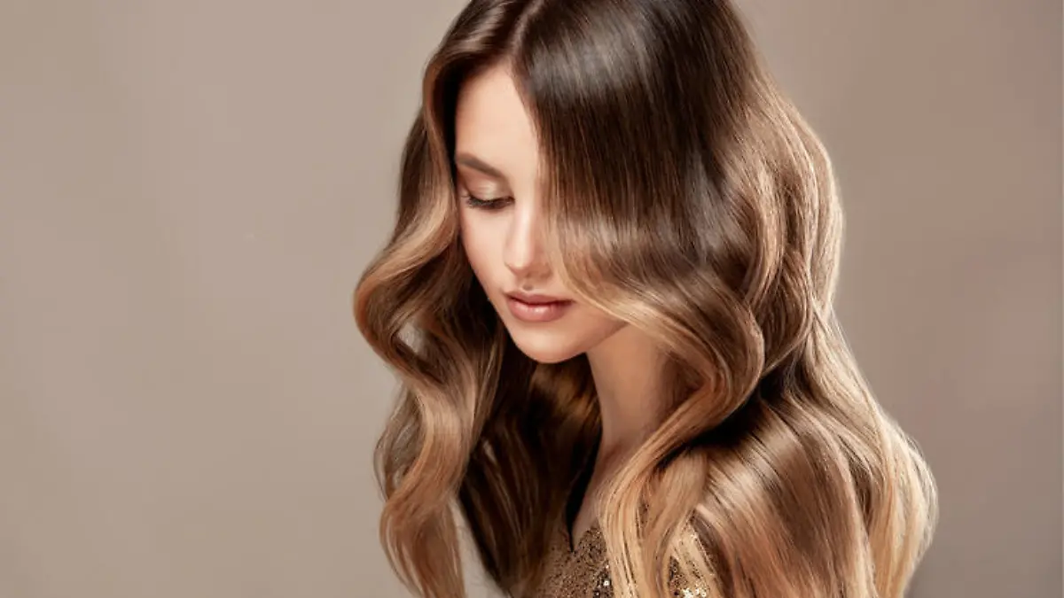 Young, beautiful brown haired woman is demonstrating wavy, dense, dyed long hair. Shades of brown color in a locks of hair. Multilayer, complex colouring of woman hair. Modern trends of hair dye. Hairdressing art and hair care.