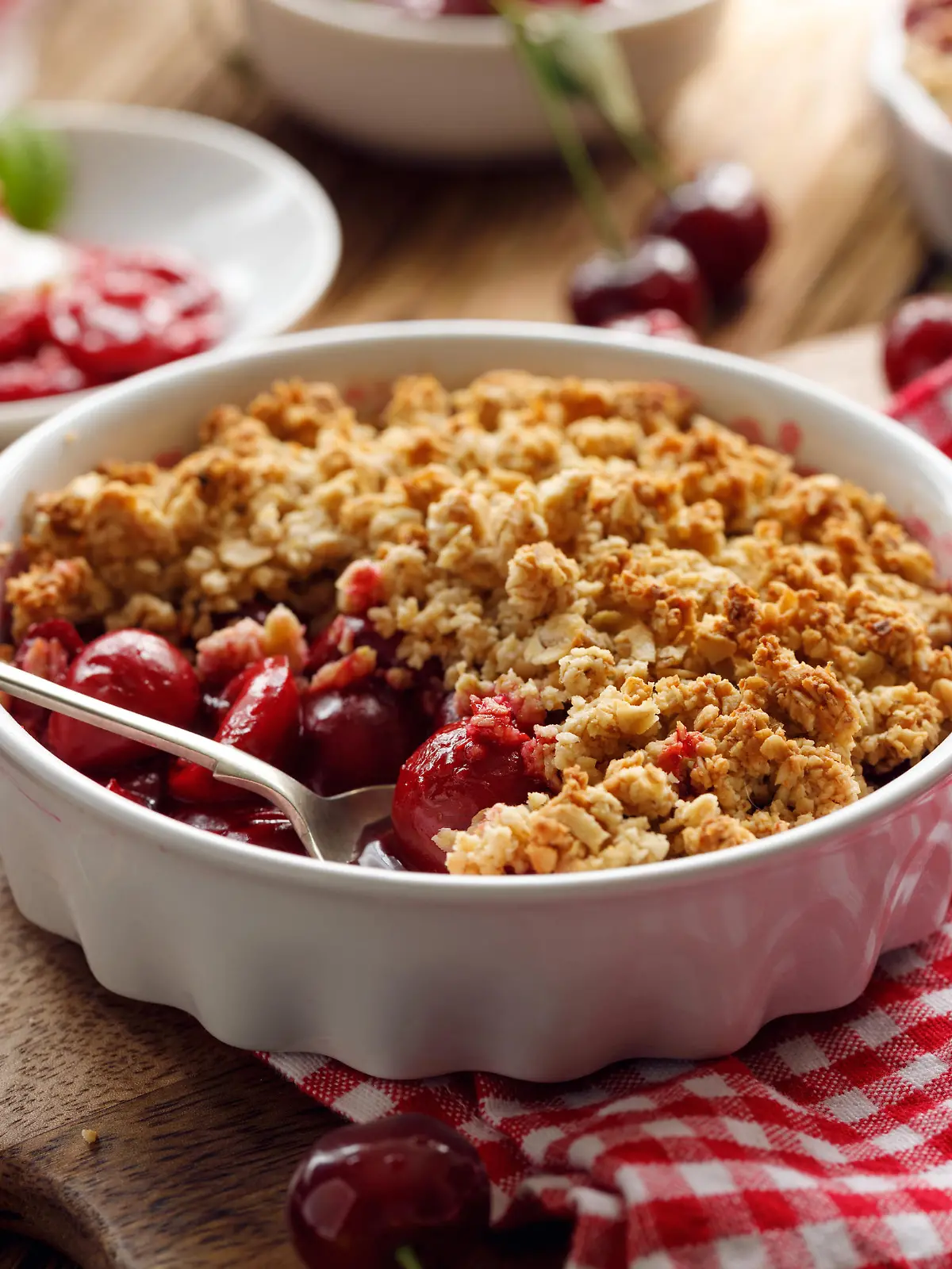 Cherry crumble, stewed fruits topped with crumble of oatmeal, almond flour, butter and sugar  in a baking dish on a wooden table, close-up