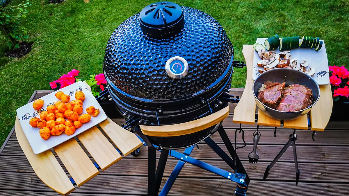 A kamado egg type barbeque grill standing on a living house terrace with beef steaks and vegetables to be cooked.