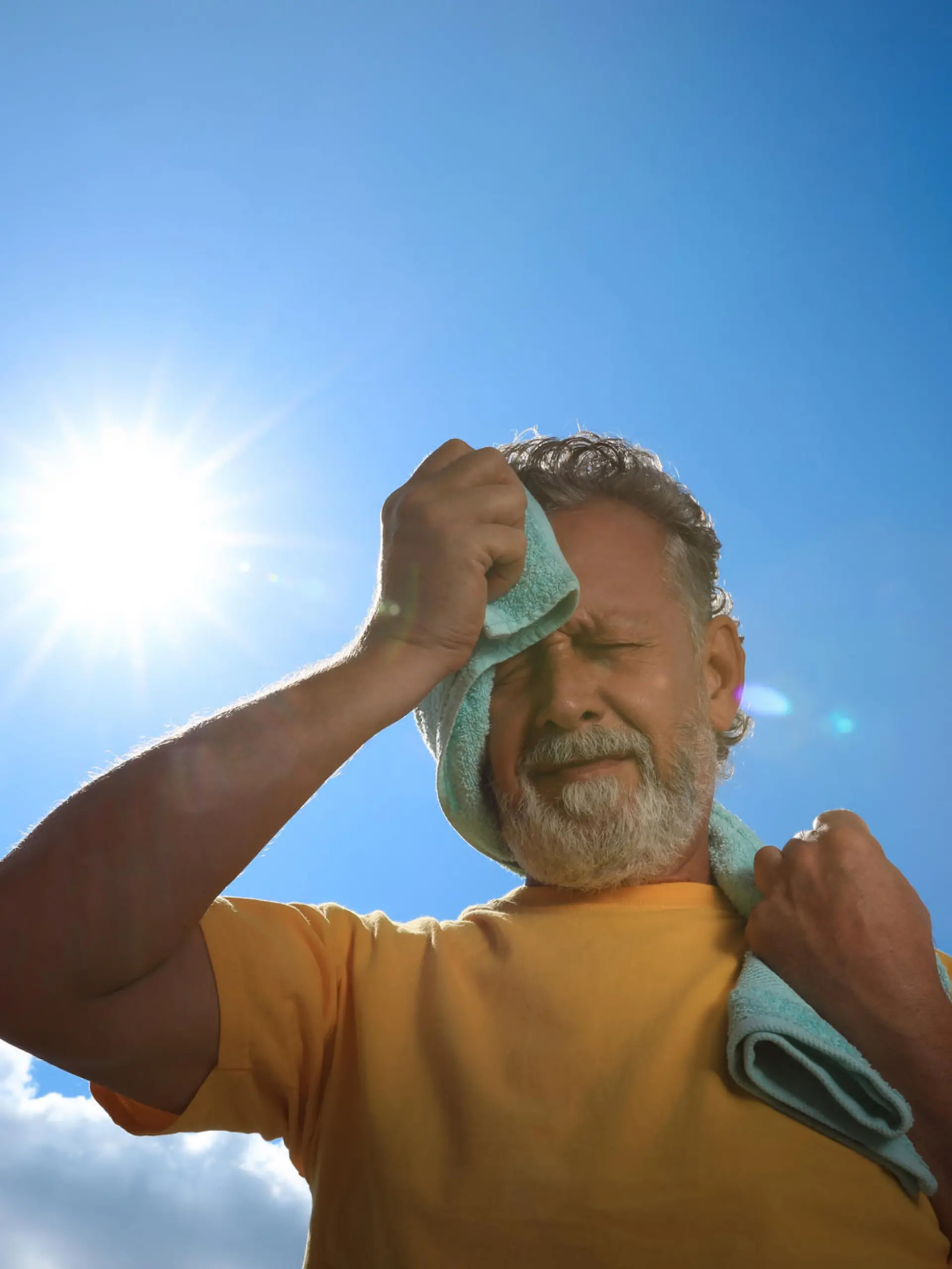 Senior man with towel suffering from heat stroke outdoors, low angle view
