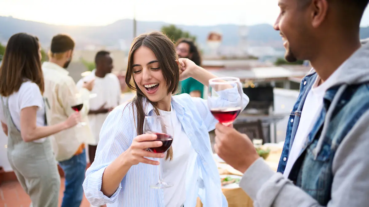 Eine junge Frau tanzt ausgelassen mit einem Glas Wein in der Hand auf einer Party.