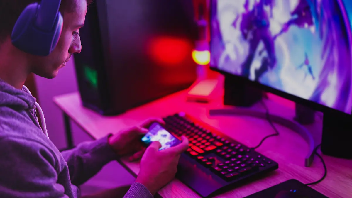 Young boy wearing headset and play video games with smartphone online in front of computer - Home isolated for coronavirus outbreak