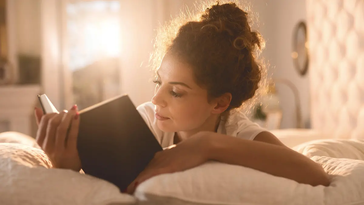Young woman lying in bed and reading a book.