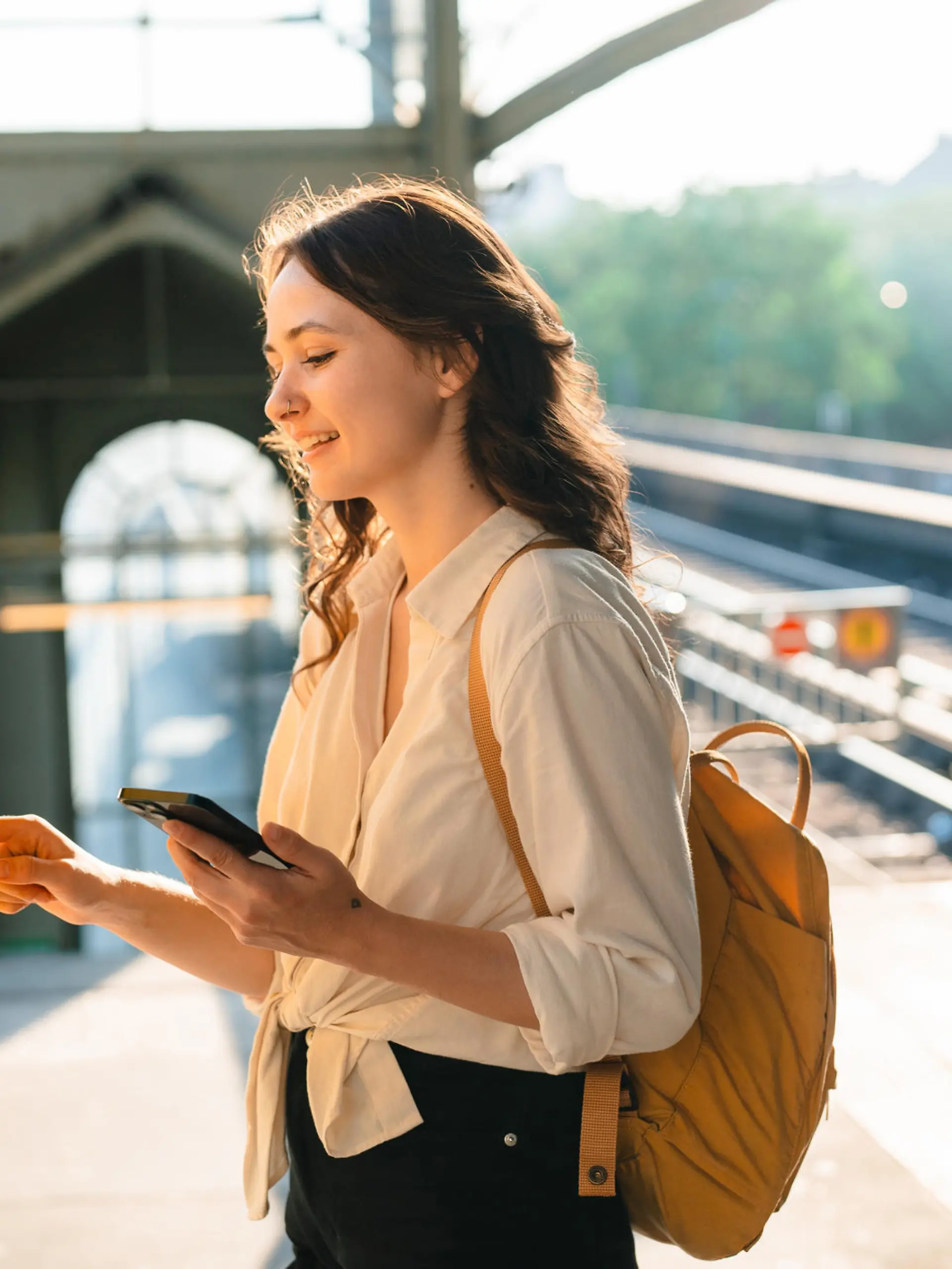 Cheerful woman buying ticket from ticket machine on the station while holding smartphone