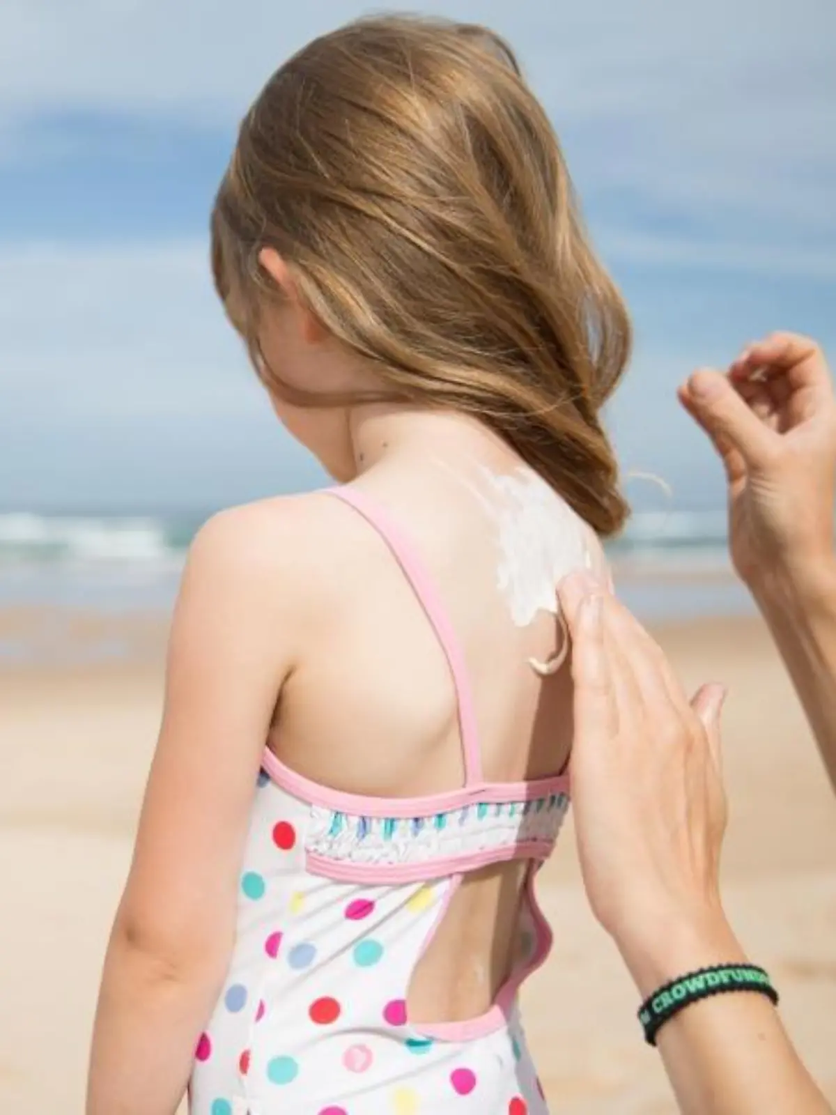Kind wird am Strand mit Sonnencreme eingecremt.