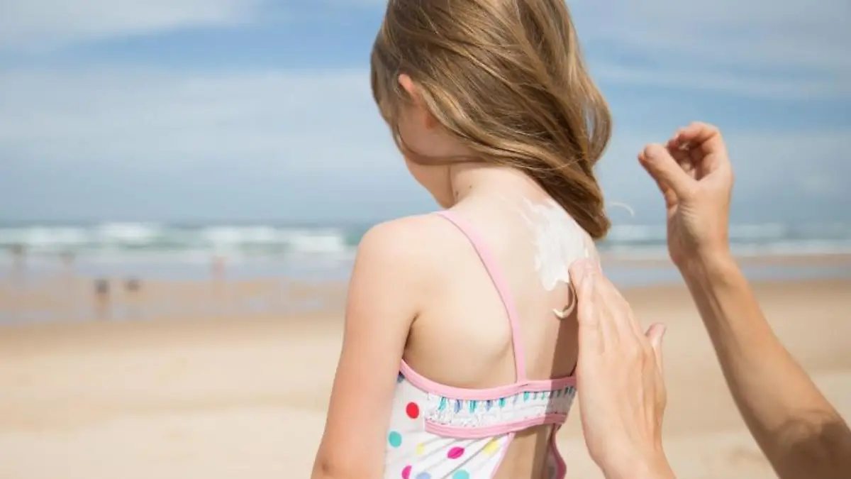 Kind wird am Strand mit Sonnencreme eingecremt.