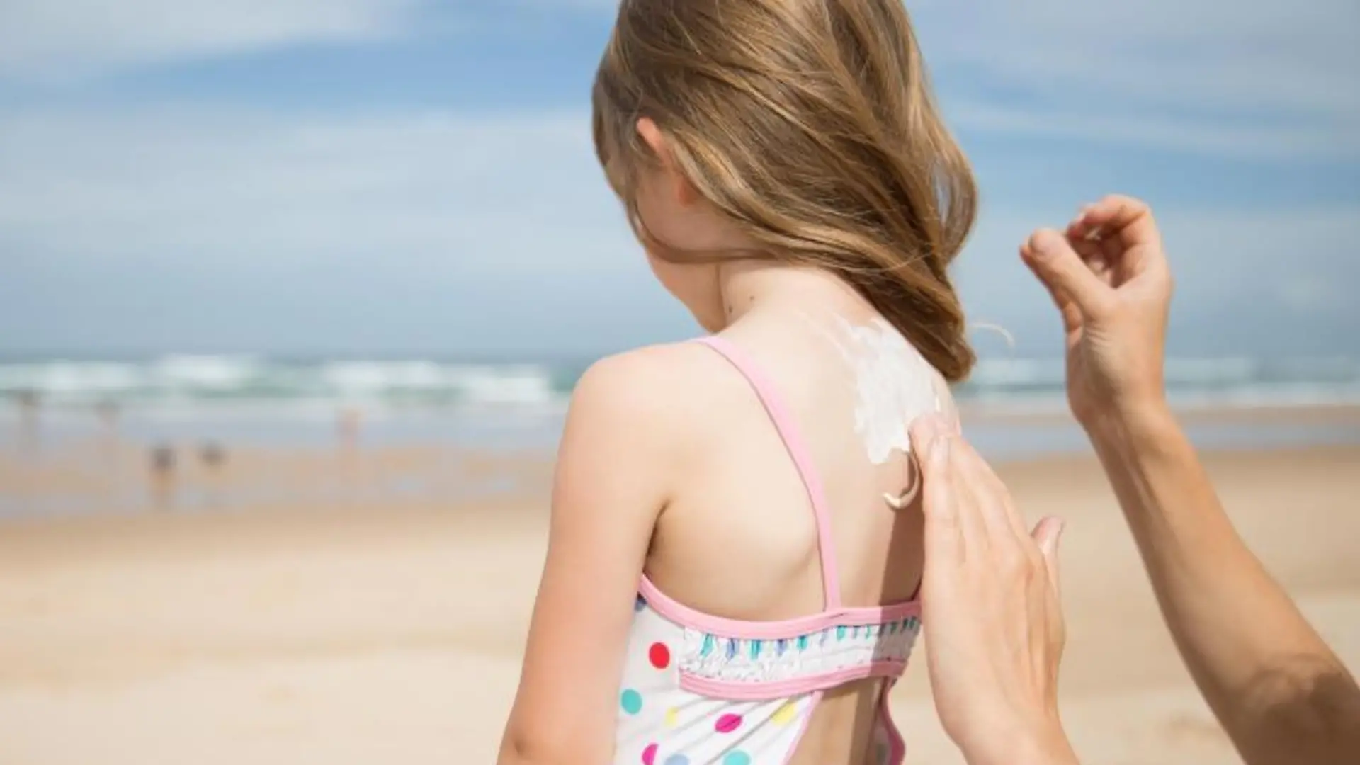 Kind wird am Strand mit Sonnencreme eingecremt.