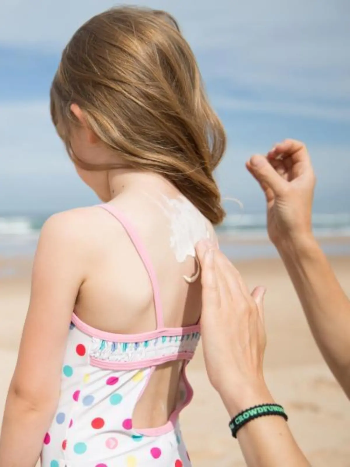 Kind wird am Strand mit Sonnencreme eingecremt.