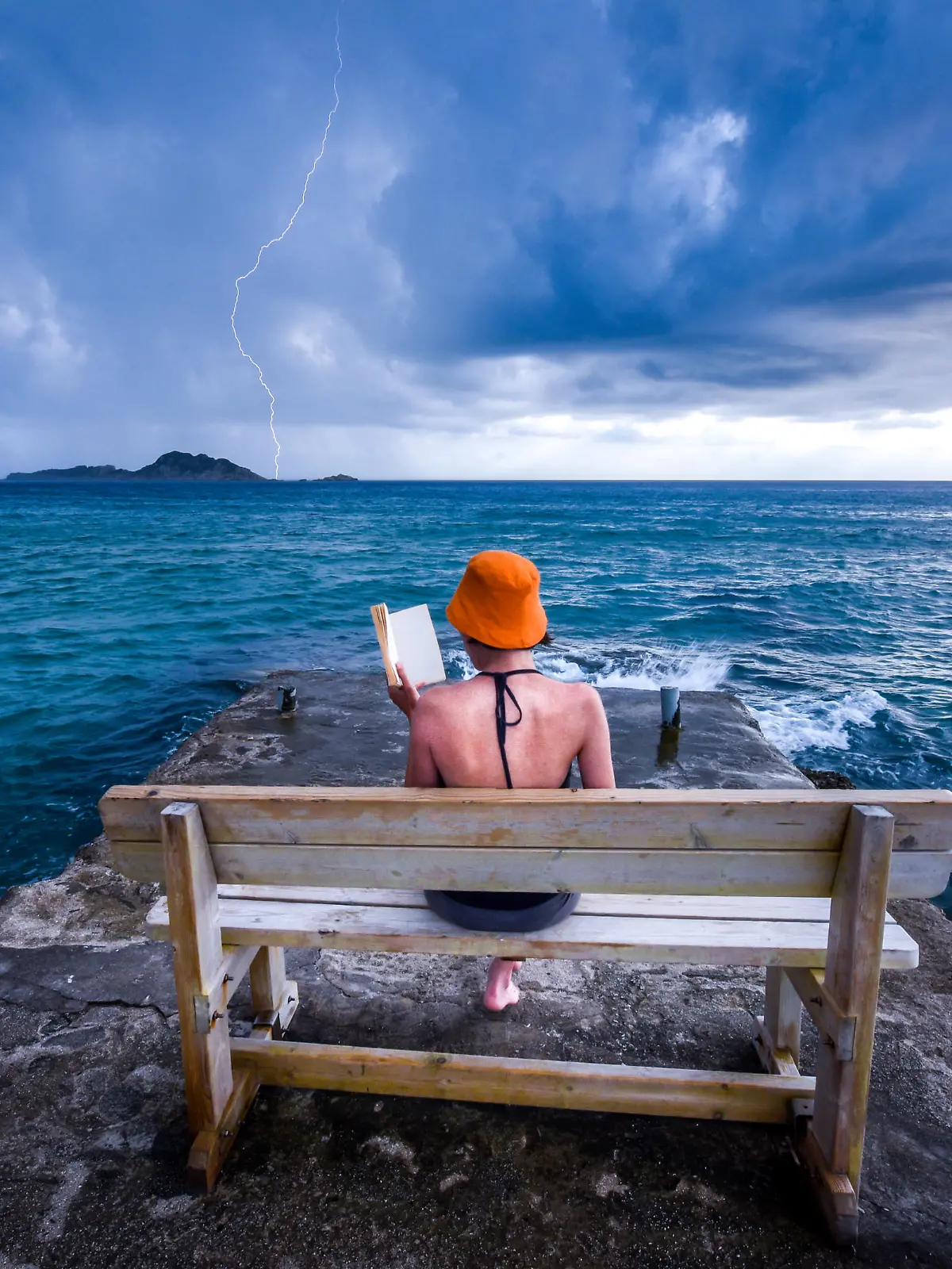 Dramatic  summer moment caught on a camera. Young woman is reading a book on a bench at a pear near the sea, while storm is approaching. Dramatic sky in the background with caught lightning