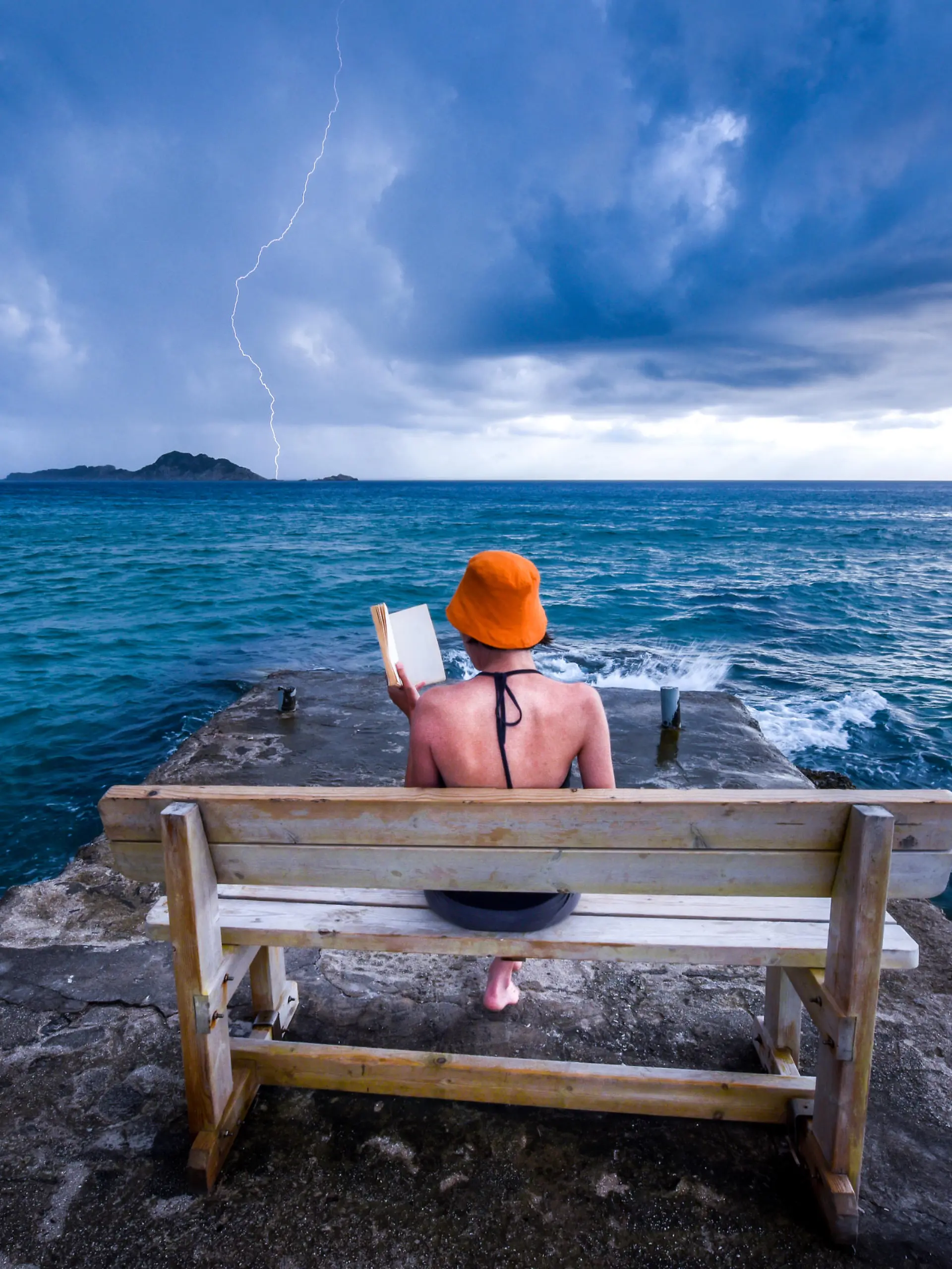 Dramatic  summer moment caught on a camera. Young woman is reading a book on a bench at a pear near the sea, while storm is approaching. Dramatic sky in the background with caught lightning