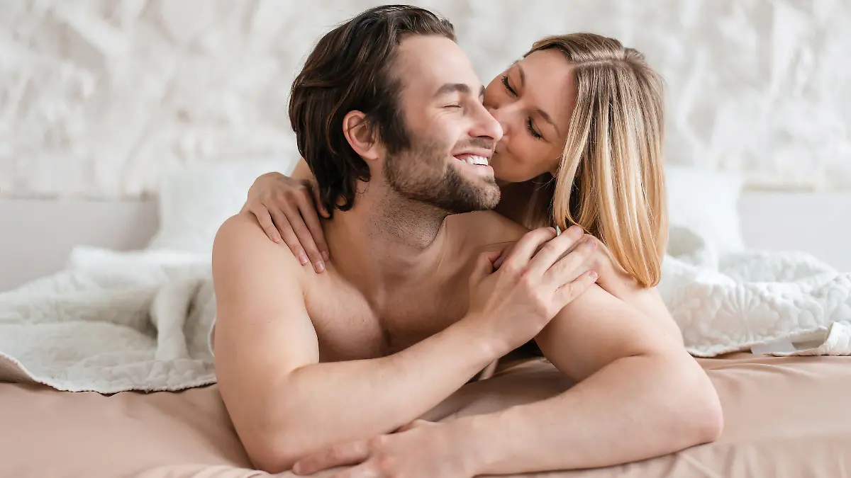 Frau küsst ihren Freund, während beide nackt im Bett liegen.
