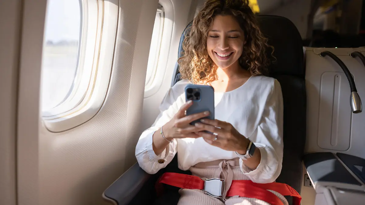 Happy Latin American woman using her cell phone in an airplane while traveling