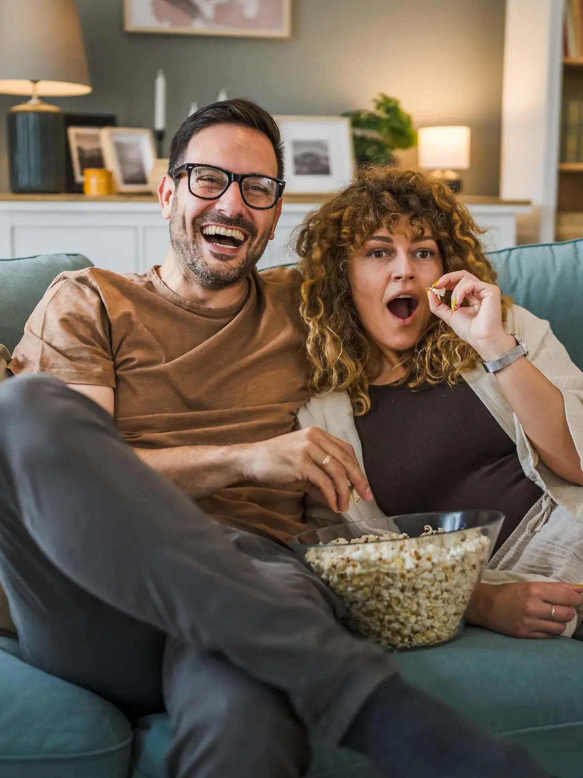 Couple man and woman caucasian husband and wife or boyfriend and girlfriend sit on the sofa bed at home watch tv movie series with bowl of popcorn happy smile bonding love family concept copy space
