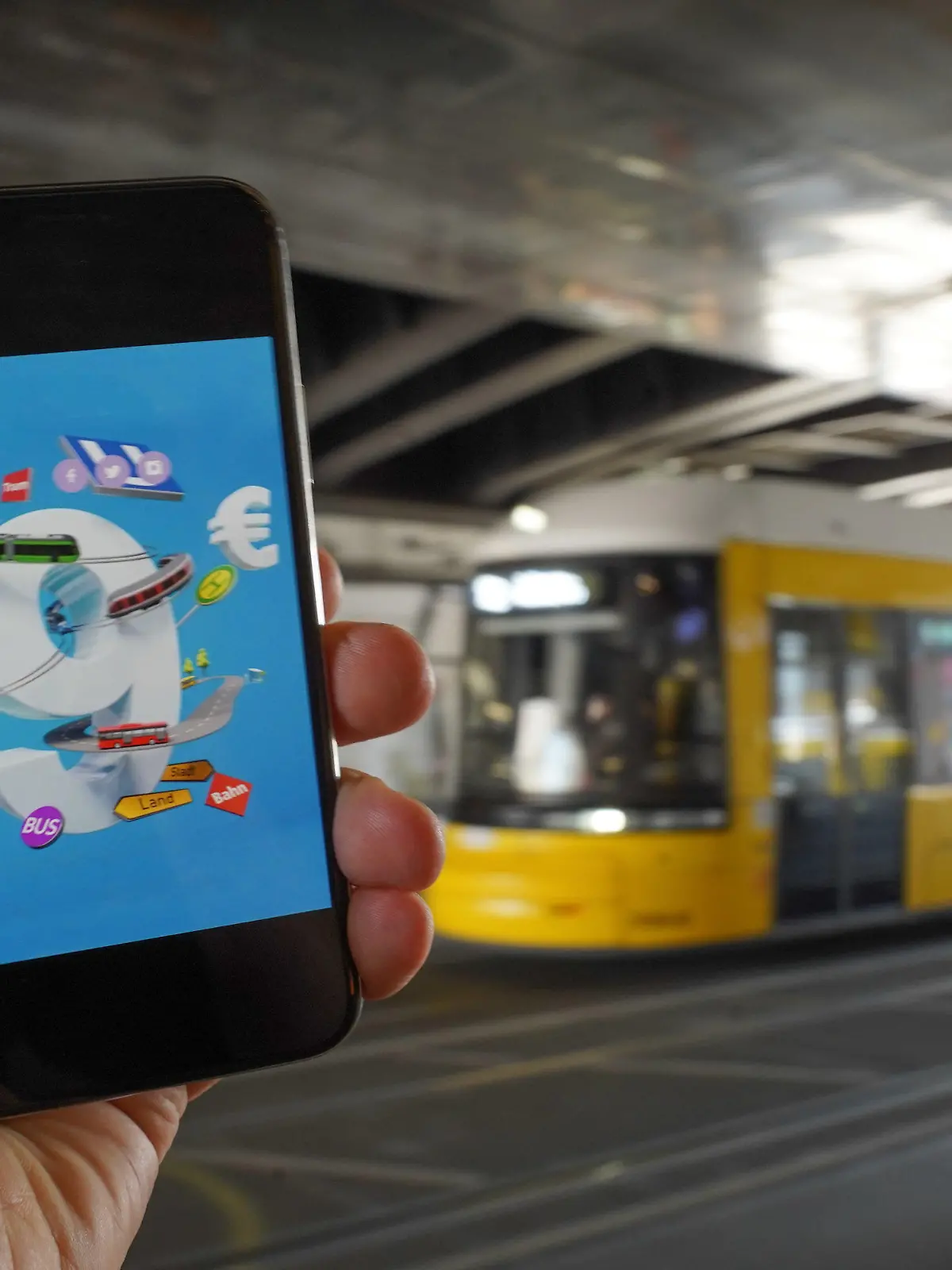 18.05.2022, Berlin: Ein Smartphone, auf dem eine Werbung für das 9-Euro-Ticket zu sehen ist, wird vor eine Tram gehalten. Die Sondertickets sollen im Juni, Juli und August bundesweit Fahrten im Nah- und Regionalverkehr ermöglichen. Der Bundestag soll das Finanzierungsgesetz an diesem Donnerstag beschließen, am Freitag soll der Bundesrat abschließend entscheiden. Foto: Jörg Carstensen/dpa +++ dpa-Bildfunk +++